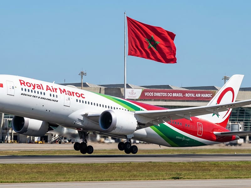 Avião da Royal Air Maroc prestes a decolar com bandeira do Marrocos ao fundo, representando a promoção de voos diretos do Brasil.